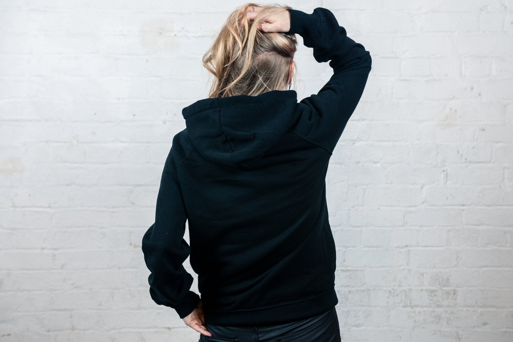 Blonde woman wearing black hoodie, back of hoodie on display