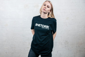Female model in studio wearing black organic T-shirt with 'Rhetorik Organic Clothing' printed on chest. 