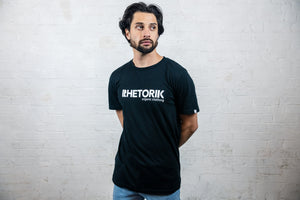 Male model in studio wearing black organic t-shirt with rhetorik text logo and organic clothing tagline printed on chest. 
