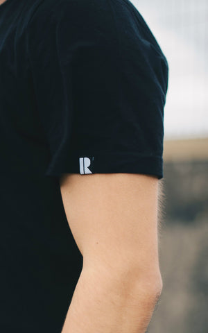 Small sleeve label with Rhetorik logo woven into organic cotton T-shirt in black. 