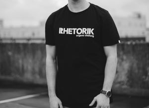 Black t-shirt with Rhetorik organic clothing printed worn by male model, cropped at neck. 